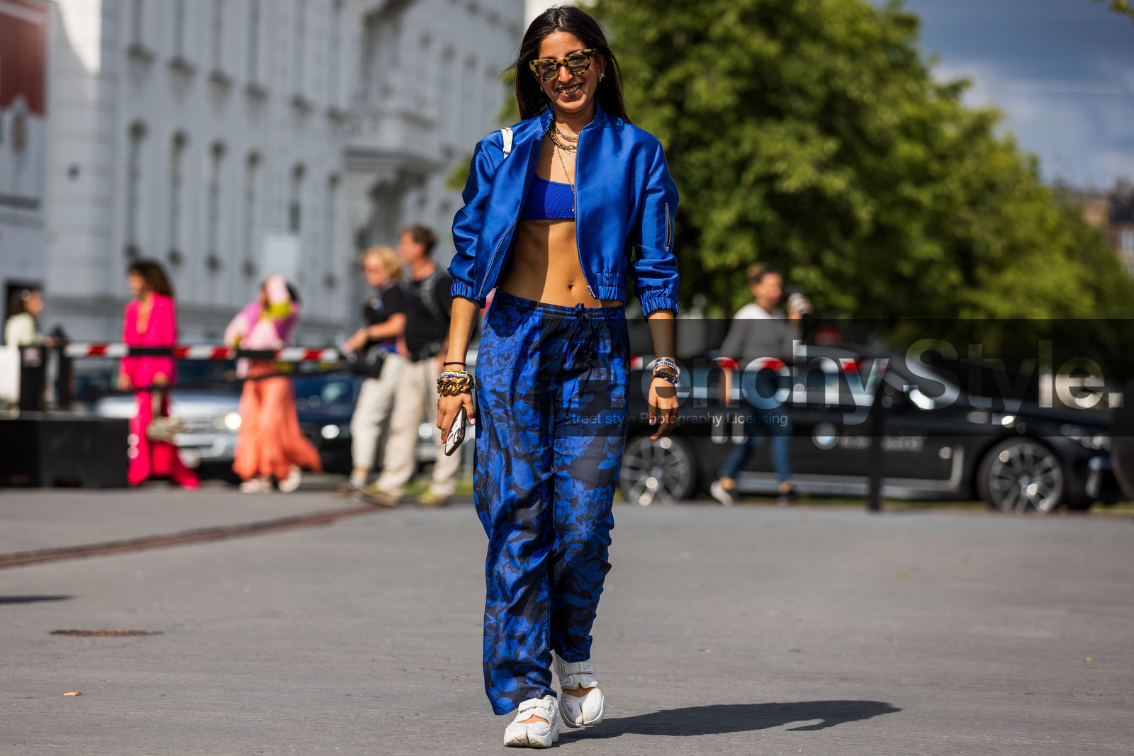 Selma Kaci, blue top, blue total look, blue bombers, blue pants, cropped top, tank top, scale sunglasses, golden necklace, multi necklace, floral printed pants, sportswear, sportswear look, jogging pants, nike shoes, white sneakers, golden bracelet, big chain bracelet, lucky charm bracelet, multicolor bracelet, pearl bracelet, fashion week, frenchystyle, FW, jonathan paciullo, street style, SPRING SUMMER 2022, SS 22, COPENHAGEN, CPHFW, atmosphere details, horizontal, full length